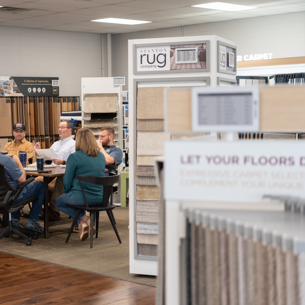 Team meeting in a flooring showroom surrounded by samples.